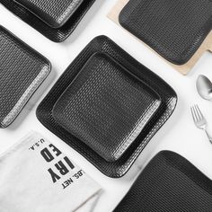 black placemats and silverware are laid out on a white surface