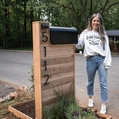 a woman standing next to a wooden mailbox