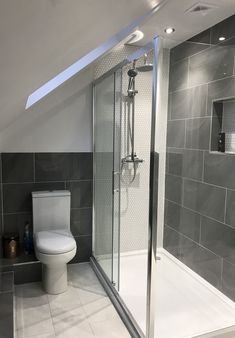 a white toilet sitting in a bathroom next to a walk in shower and tiled walls