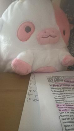 a pink and white stuffed animal sitting on top of a table next to a piece of paper