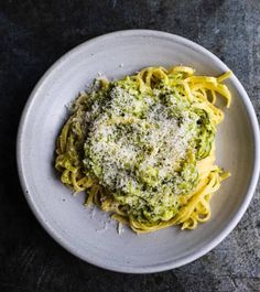 a white plate topped with pasta covered in pesto sauce and parmesan cheese