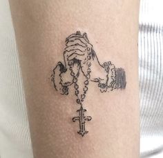 a woman's arm with a tattoo on it that has a cross and hands holding beads