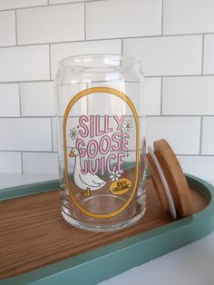 a glass with the words silly goose juice on it next to a wooden lid and coaster