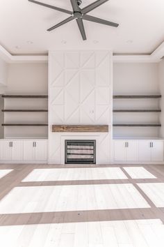 an empty living room with white walls and ceiling fan in the center, surrounded by shelving units