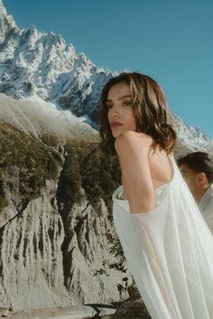 a woman wearing a white dress standing in front of a mountain