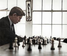 a man sitting at a table with chess pieces in front of him and looking down