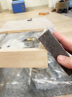 a person holding a piece of wood in their hand and sanding it on the floor