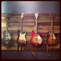 four guitars are lined up on a wall