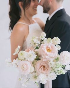 a bride and groom standing next to each other in front of a white wall holding a bouquet of flowers