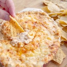 a person dipping tortilla chips into a white dish with cheese and sauce on it