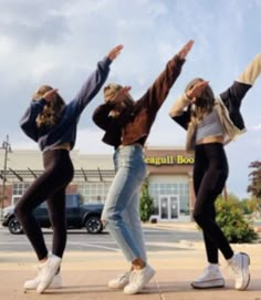 four young women are dancing in front of a store with their arms up and hands out