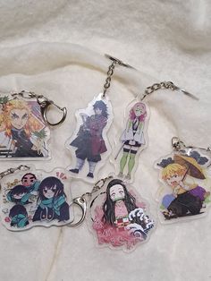 six keychains with anime characters on them sitting on a white cloth covered surface