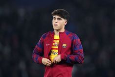 a young man standing on top of a soccer field wearing a red and blue uniform