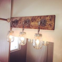 three mason jar lights are hanging from a wooden beam above a mirror in a bathroom