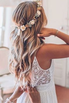 a woman with long hair wearing a white dress and flowers in her hair is looking back at the camera