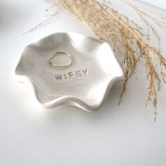 a silver ring dish with the word wife written on it next to some dried grass