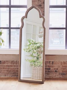 a mirror sitting on top of a wooden floor next to a brick wall and window