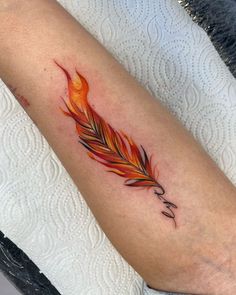 an orange and red feather tattoo on the arm