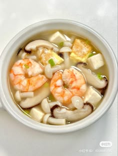 a bowl of soup with shrimp, tofu and mushrooms in it on a white table