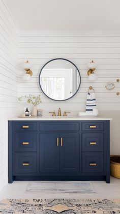 a bathroom with white walls and blue cabinetry, gold hardware on the drawers and a round mirror above it