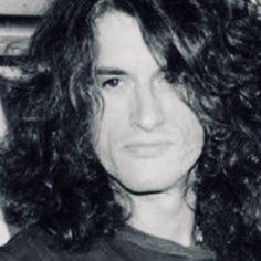 a black and white photo of a man with long hair wearing a t - shirt