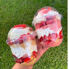 two desserts in plastic containers with strawberries and other toppings on the grass