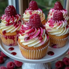 cupcakes with raspberries and cream frosting on a cake plate