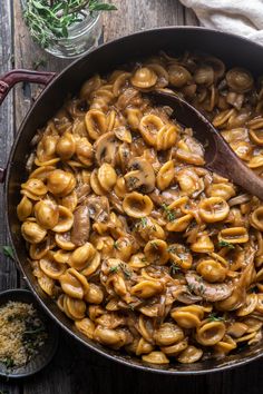 a skillet filled with pasta and mushrooms on top of a wooden table next to other dishes