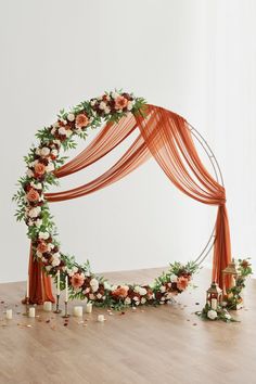 an orange and white wedding arch decorated with flowers, greenery and candles on a wooden floor