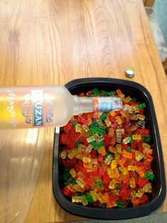 a plastic container filled with gummy bears on top of a wooden table next to a bottle of water