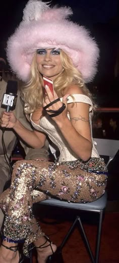 a woman sitting on top of a chair wearing a pink hat and holding a microphone