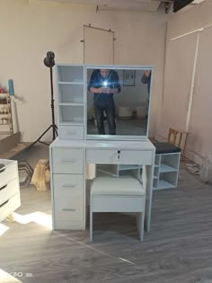 a man is taking a selfie in front of a white desk with drawers and shelves