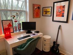 a desk with a keyboard, monitor and guitar in front of a window that has pictures on it