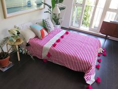 a pink and white striped bed with pom - poms on the bottom cover