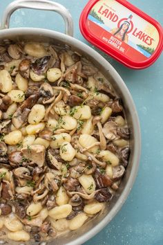 a pan filled with pasta and mushrooms on top of a blue table next to a red container