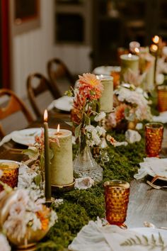 the table is set with candles, plates and flowers in vases on mossy ground