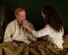 a man and woman sitting on top of a bed in front of a green wall