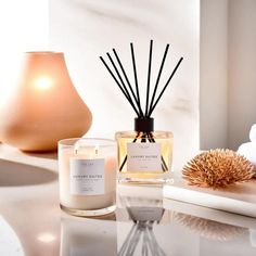 an assortment of candles on a table next to a vase with flowers and a candle