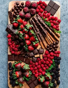 an assortment of chocolates, strawberries and berries on a cutting board with mint leaves