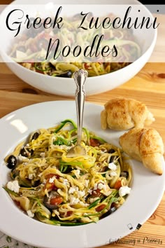 a white plate topped with pasta and vegetables next to croissants on a wooden table