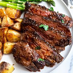 a white plate topped with steak, potatoes and asparagus next to a fork