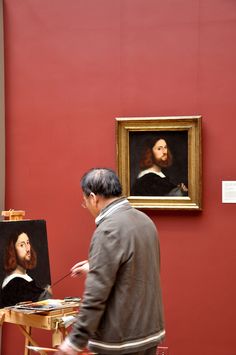 a man standing in front of a painting on a easel next to a red wall