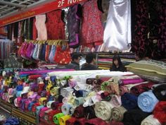 there are many different fabrics on display at this market stall, including ties and scarves