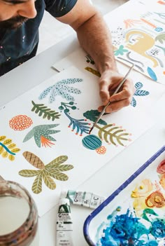 a man is painting flowers on paper with watercolors