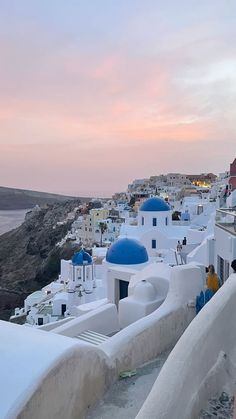 the sky is pink and blue as people walk on top of white buildings in oia