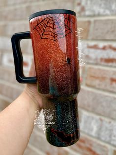 a hand holding a red and black coffee mug with spider webs on the side