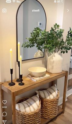 a wooden table topped with a vase filled with flowers next to a mirror and two wicker baskets