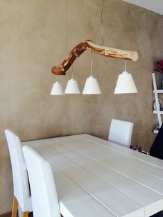 a dining room table with white chairs and a wooden branch hanging from it's ceiling