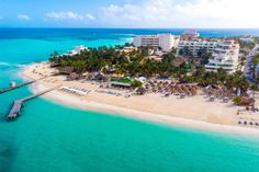 an aerial view of a resort and beach with palm trees in the foreground, surrounded by clear blue water