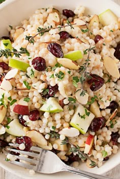 a white bowl filled with rice, nuts and cranberries next to a fork